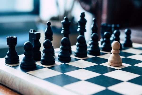 Representation of a business leader facing impossible odds. Single pawn stands against an entire chess board.