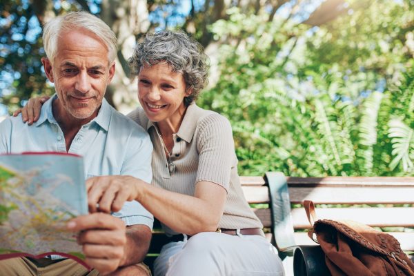 Portrait of happy man and woman reading map while sitting on a park bench. Senior couple on vacation using city map.